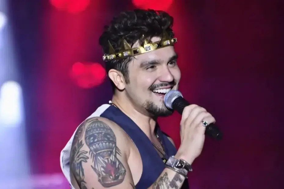Luan Santana sorrindo com microfone e coroa dourada durante o show Registro Histórico na Arena MRV.