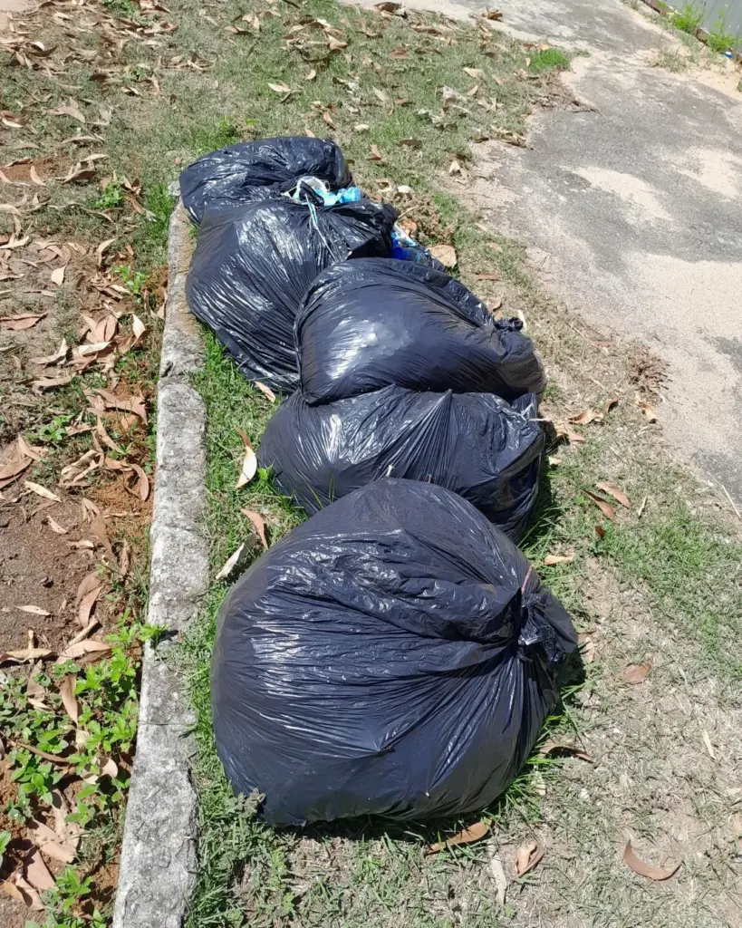 Sacos de lixo pretos acumulados sobre a grama na calçada no bairro Nova Guarapari, evidenciando problemas na limpeza urbana em Guarapari.