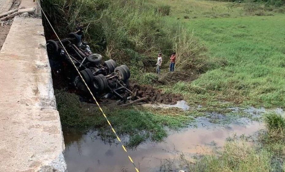 Caminhão acidentado na ponte em Minas Gerais; motorista faleceu. Bombeiros aguardam perícia para remoção do corpo.