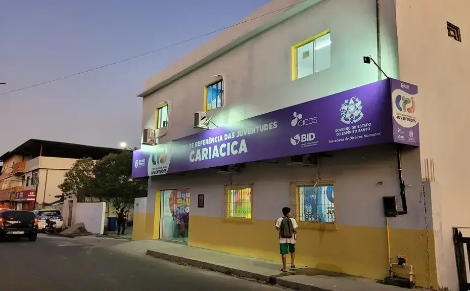 Centro de Referência das Juventudes de Cariacica com placa de suspensão de atividades em frente ao prédio.