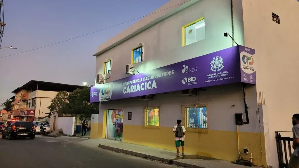 Centro de Referência das Juventudes de Cariacica com placa de suspensão de atividades em frente ao prédio.