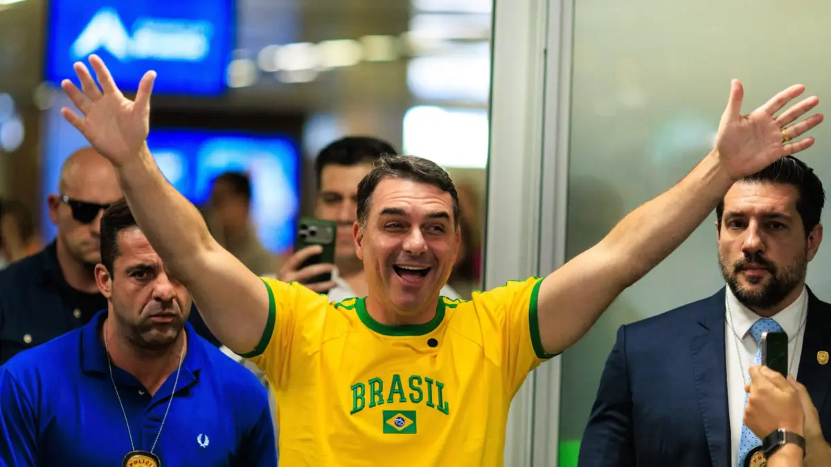 Flávio Bolsonaro durante evento de campanha presidencial, cercado por apoiadores e com expressão preocupada.
